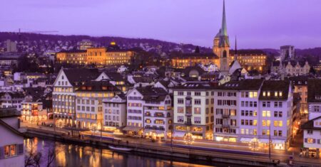 Zürich bei Abenddämmerung: beleuchtete Altstadt spiegelt sich im Fluss